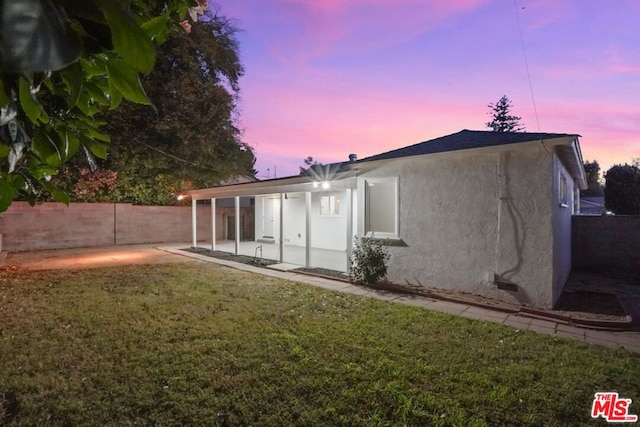 back house at dusk with a yard and a patio