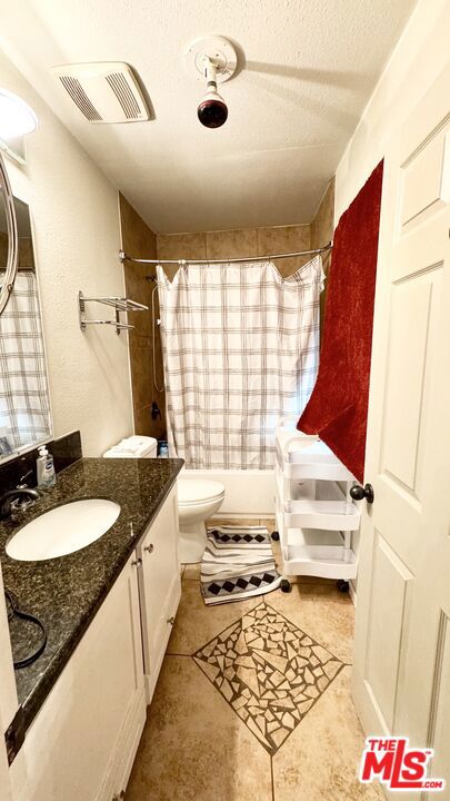 bathroom with tile patterned floors, a shower with curtain, vanity, a textured ceiling, and toilet