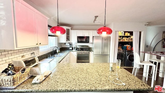 kitchen with washing machine and clothes dryer, sink, stainless steel appliances, pendant lighting, and white cabinets