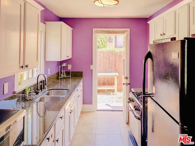 kitchen featuring black refrigerator, white cabinets, dark stone counters, and sink