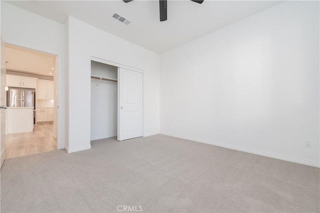 unfurnished bedroom with ceiling fan, a closet, light carpet, and stainless steel refrigerator