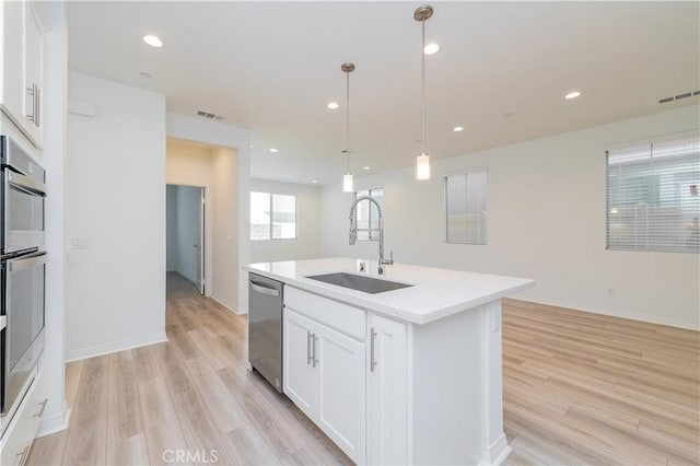 kitchen with a center island with sink, stainless steel appliances, pendant lighting, white cabinets, and sink