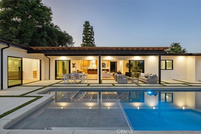 pool at dusk featuring a patio area and an outdoor living space