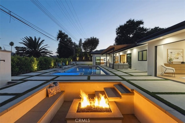 pool at dusk with an outdoor living space with a fire pit and a patio