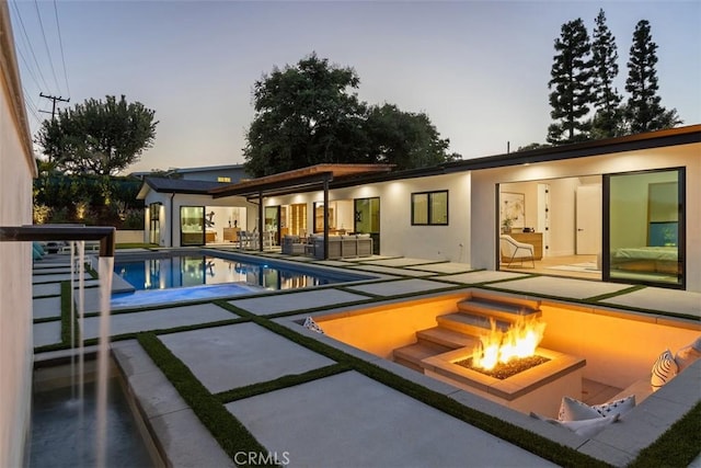 pool at dusk with an outdoor living space with a fire pit and a patio area