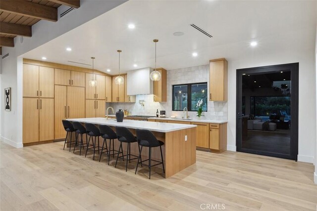 kitchen featuring beamed ceiling, light brown cabinetry, light hardwood / wood-style flooring, and a kitchen island with sink