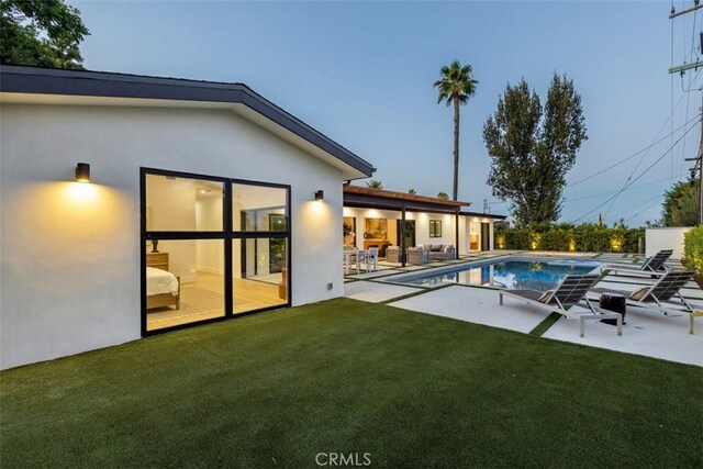 pool at dusk with a patio area and a lawn