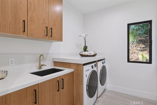 clothes washing area with cabinets, washer and dryer, and sink