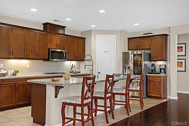 kitchen featuring appliances with stainless steel finishes, an island with sink, sink, a kitchen breakfast bar, and light stone counters