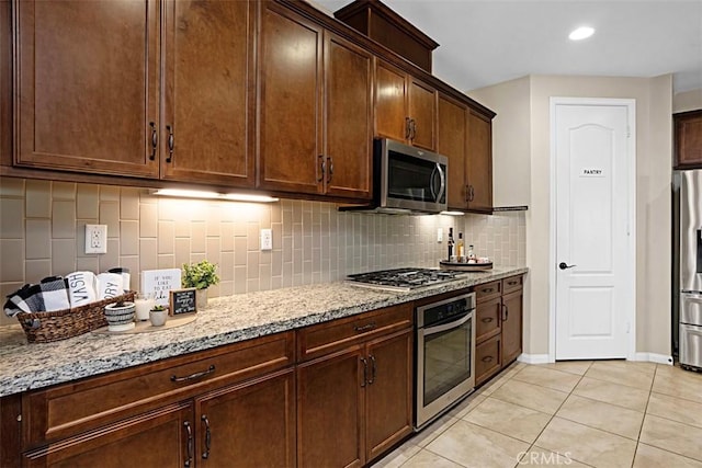 kitchen with light tile patterned floors, backsplash, light stone countertops, and appliances with stainless steel finishes