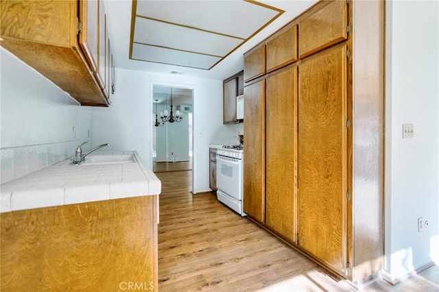 kitchen with tile counters, white appliances, a chandelier, light hardwood / wood-style flooring, and sink