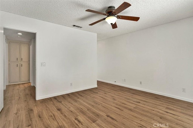 empty room featuring a ceiling fan, visible vents, baseboards, a textured ceiling, and wood finished floors