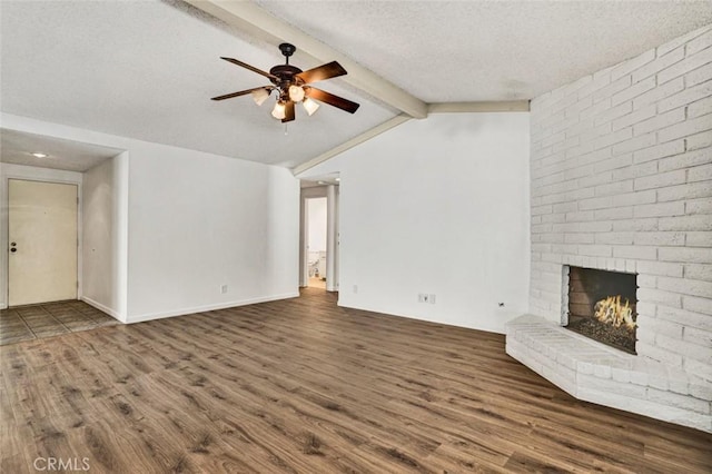 unfurnished living room with a textured ceiling, ceiling fan, dark hardwood / wood-style floors, lofted ceiling with beams, and a brick fireplace