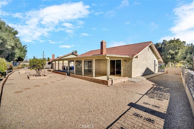 rear view of house featuring a chimney, stucco siding, fence, a patio, and a tile roof