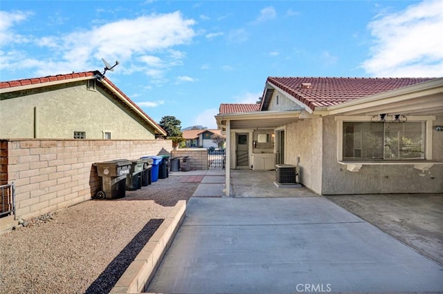 view of side of home with central AC, stucco siding, a tiled roof, and fence