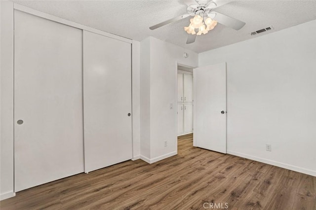 unfurnished bedroom featuring ceiling fan, a closet, a textured ceiling, and hardwood / wood-style flooring