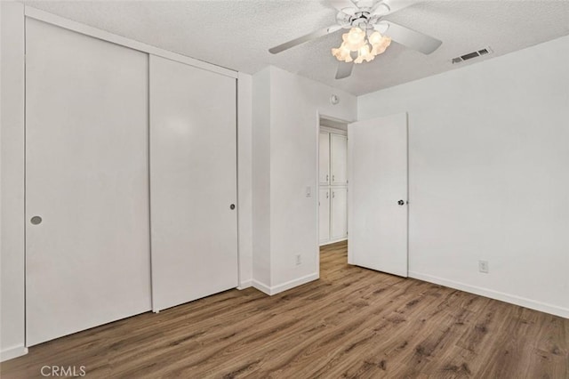 unfurnished bedroom with a textured ceiling, visible vents, a closet, and wood finished floors