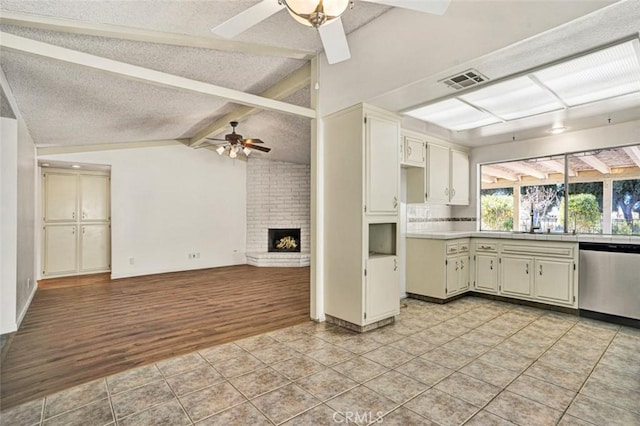 kitchen featuring a fireplace, a textured ceiling, stainless steel dishwasher, and vaulted ceiling with beams