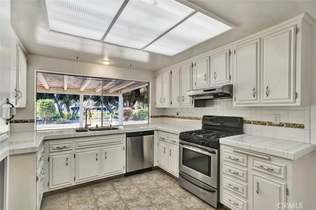 kitchen with white cabinets, stainless steel appliances, sink, backsplash, and light tile patterned floors