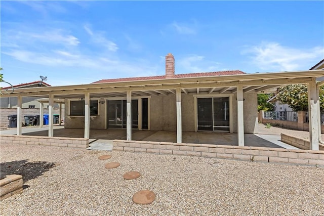 rear view of property featuring stucco siding, a tiled roof, a chimney, and a patio area