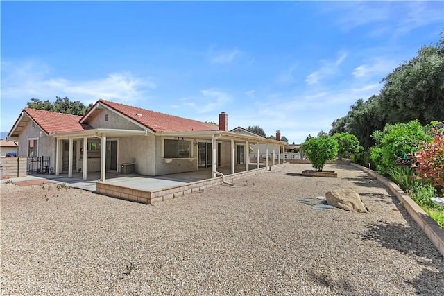 rear view of house with a chimney, fence, stucco siding, and a patio area