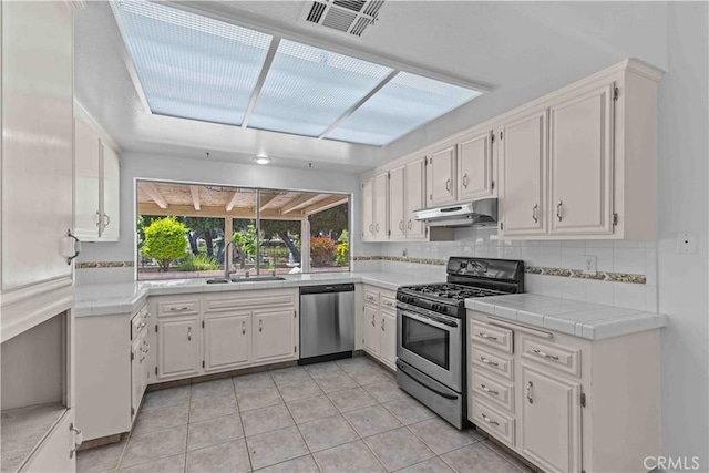 kitchen featuring a sink, under cabinet range hood, tasteful backsplash, visible vents, and appliances with stainless steel finishes