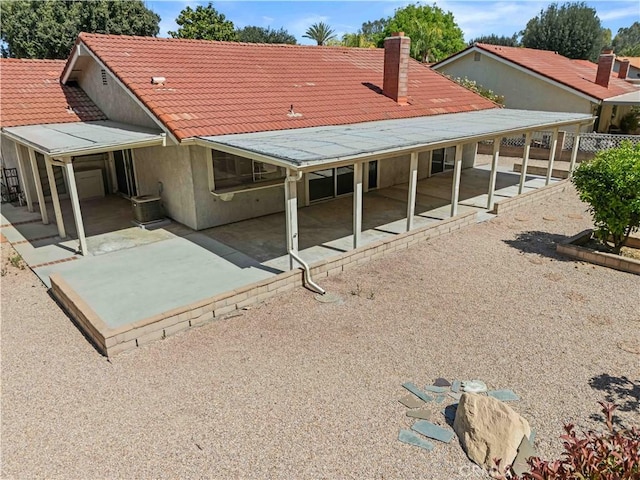 rear view of property with a tile roof, a patio area, a chimney, stucco siding, and fence