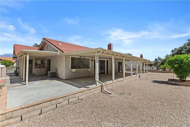 rear view of house with a tile roof, fence, a chimney, and a patio area