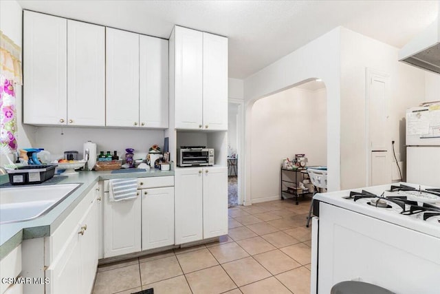 kitchen with light tile patterned floors, sink, white appliances, and white cabinetry