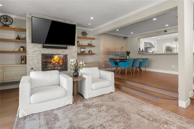 living room with crown molding, a stone fireplace, light wood-type flooring, and built in shelves