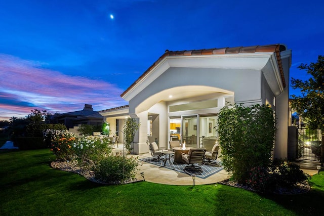 back house at dusk featuring a yard and a patio area