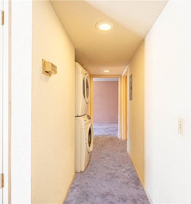 corridor featuring light carpet, a textured ceiling, and stacked washer / dryer