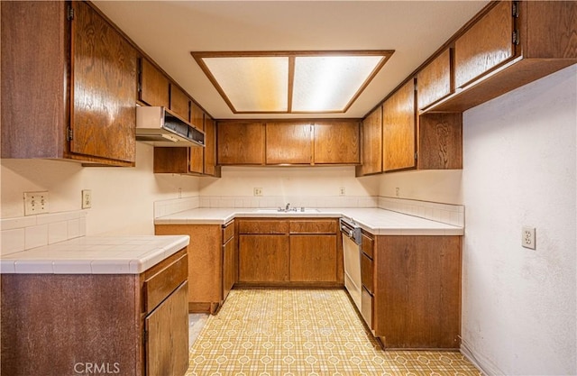 kitchen featuring exhaust hood, dishwasher, sink, and tile countertops