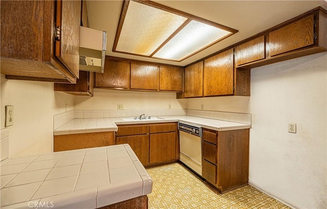 kitchen featuring tile counters, dishwashing machine, and sink