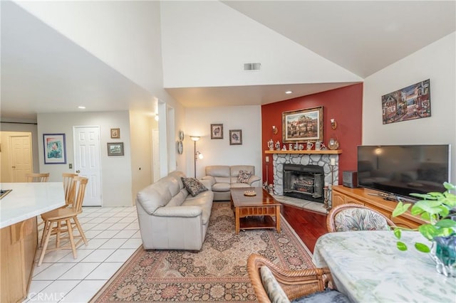 living room featuring light tile patterned floors, vaulted ceiling, and a stone fireplace