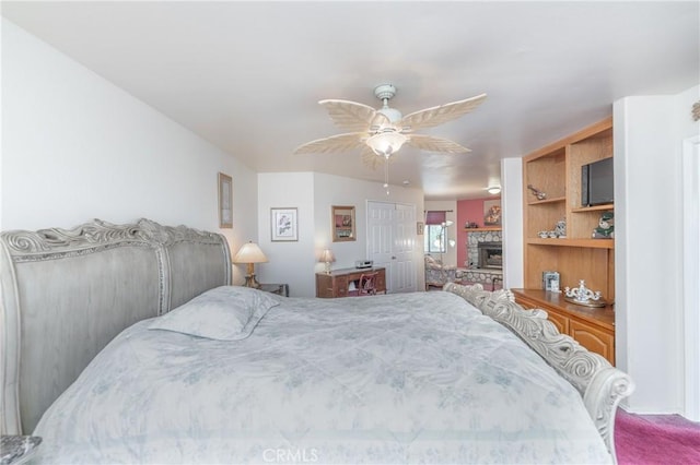 bedroom featuring ceiling fan, carpet, and a stone fireplace