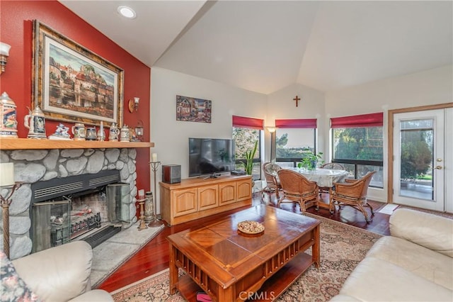 living room with light hardwood / wood-style flooring, a stone fireplace, and vaulted ceiling