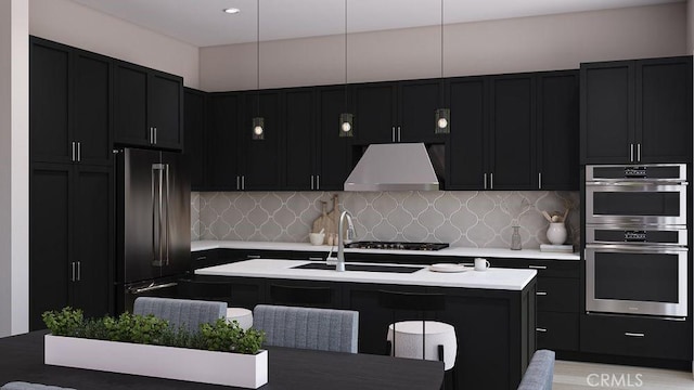 kitchen featuring ventilation hood, stainless steel appliances, tasteful backsplash, a kitchen island with sink, and sink