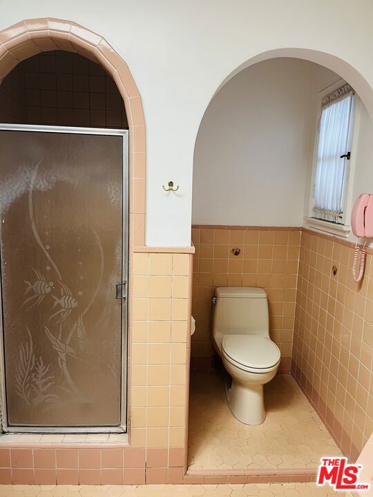 bathroom featuring toilet, a shower, tile walls, and tile patterned floors