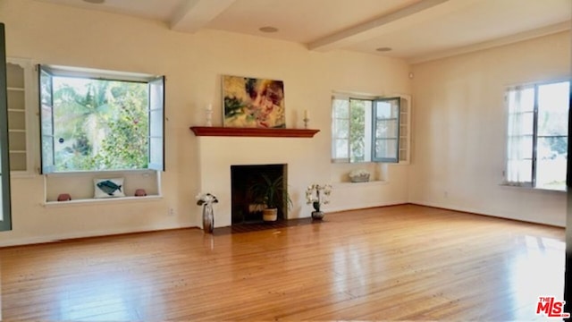 unfurnished living room featuring a healthy amount of sunlight, light hardwood / wood-style floors, and beam ceiling