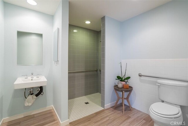 bathroom featuring toilet, tile walls, wood-type flooring, and tiled shower