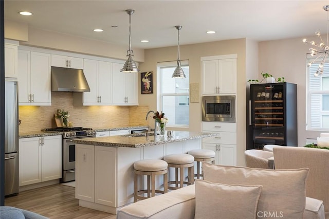 kitchen with decorative light fixtures, sink, appliances with stainless steel finishes, an island with sink, and dark stone counters