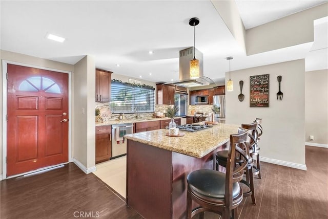 kitchen with light stone countertops, pendant lighting, island exhaust hood, stainless steel appliances, and tasteful backsplash