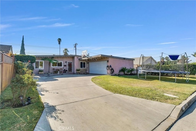 ranch-style home with a garage, a front lawn, and a trampoline