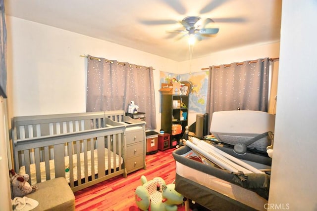 bedroom featuring ceiling fan, a crib, and hardwood / wood-style flooring