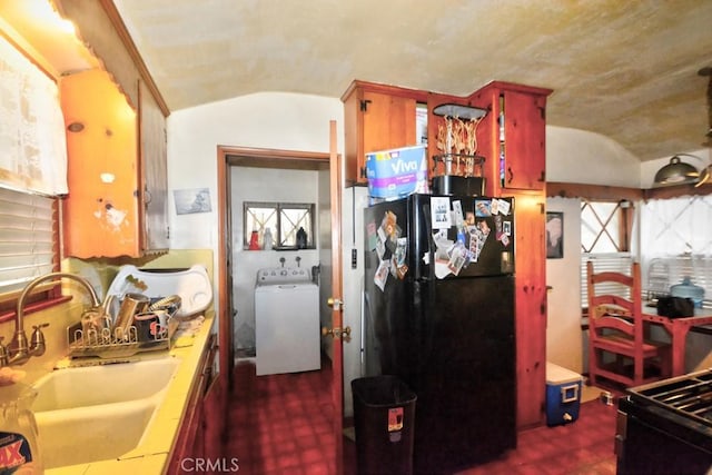 kitchen featuring vaulted ceiling, washer / clothes dryer, sink, black refrigerator, and tile counters