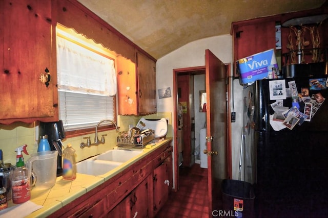 kitchen featuring sink, black fridge, lofted ceiling, and tile countertops