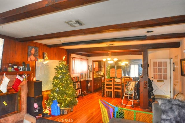 dining space with wood walls, wood-type flooring, beam ceiling, and an inviting chandelier