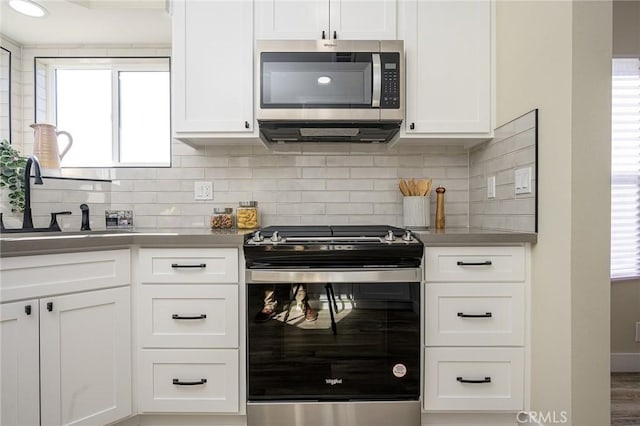 kitchen featuring stainless steel appliances, a healthy amount of sunlight, white cabinets, and tasteful backsplash