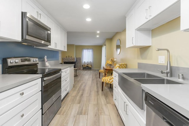 kitchen with white cabinets, appliances with stainless steel finishes, light wood-type flooring, and sink